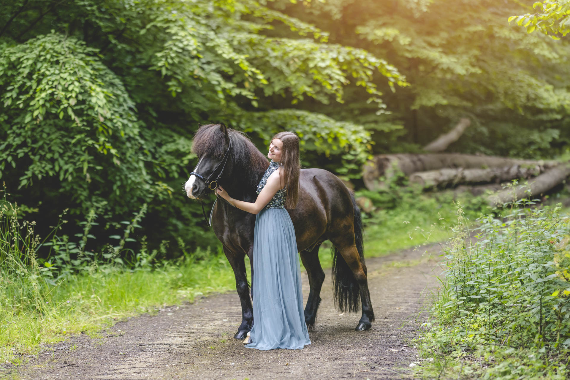 Pferdemädchen im blauen Kleid steht neben einem Isländer